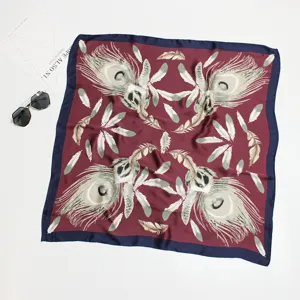 Elegant square silk-like scarf with peacock feather pattern on burgundy background.