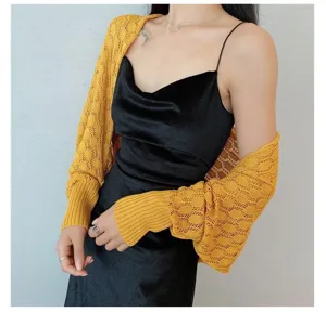 Detailed view of yellow hollowed-out knitted shrug bolero worn over a black camisole dress