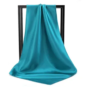 Detail showing the elegant drape and shiny satin texture of a peacock blue square scarf