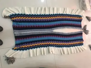 Detailansicht eines bunten Strickponchos mit Zickzackmuster, Quasten und Rüschenrand