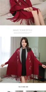 Dettaglio di un poncho rosso in maglia con ricamo floreale e frange eleganti