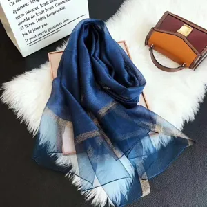 Eleganter blauer Seiden-Wollschal mit Goldrand auf einem weißen Kunstfellhintergrund.
