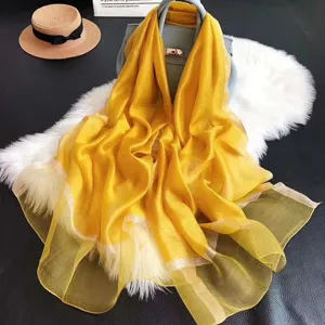 Eleganter leuchtend gelber Seiden-Wollschal mit Goldbesatz über einer schicken Handtasche