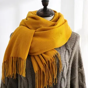 Close-up of mustard yellow thick knit scarf with long tassels draped on a mannequin