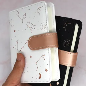 Primer plano de libreta con tema celestial, diseño de constelaciones y cierre oro rosa.