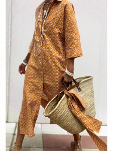 Detail shot of a women's orange geometric print shirt dress styled with a straw tote