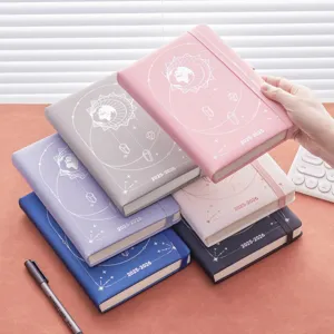 Agenda académica 2025-2026 con diseño celeste de sol y tierra en varios colores sobre mesa.