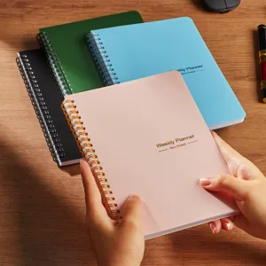 Primo piano di mani che tengono un planner settimanale rosa A5 con spirale.