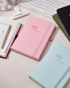 Agende giornaliere 2026 in rosa e blu disposte su una scrivania con vari accessori