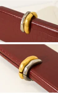 Detalle de bolso de mano granate con textura de cocodrilo y cierre de metal bicolor.
