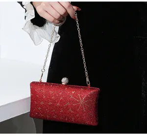 Elegante rote Abendtasche mit Strasssteinen und goldener Kette, von einem Model gehalten.