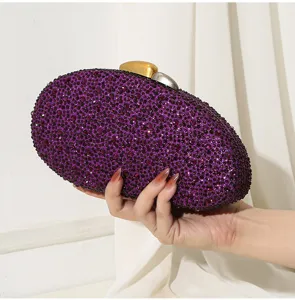 Nahaufnahme einer Hand, die eine lila Abendtasche mit funkelndem Strassstein hält.