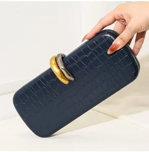 Elegante bolso de mano azul marino con estampado de cocodrilo y anillos metálicos cruzados.