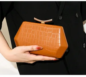 Detail einer braunen Hexagon-Clutch mit Krokoprägung und elegantem goldenen Metallverschluss.