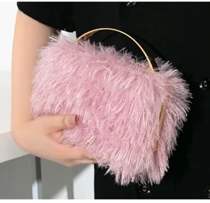 Makrodetail einer rosa Abendtasche aus Fransenplüsch mit goldenem Metallgriff in der Hand