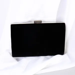 Elegant black velvet evening clutch bag with sleek metallic clasp on draped white fabric background