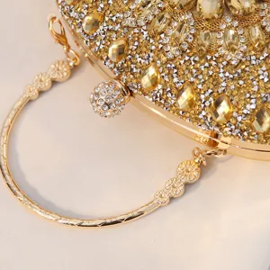 Detailaufnahme einer goldfarbenen, strassbesetzten Abendtasche mit rundem Metallgriff.