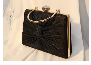 Detailansicht einer schwarzen Abendtasche mit Goldgriff und Kristallverschluss.