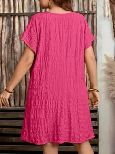 Back view of a loose fuchsia short-sleeved dress showing pleated texture and rustic background