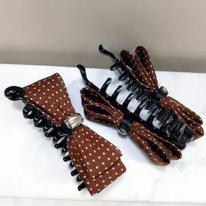 Detailed view of brown polka dot bow hair clips with crystal accent on white marble.