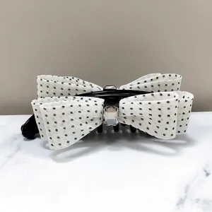 Detail view of an elegant white polka dot bow banana hair clip with a sparkly crystal center