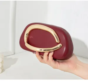 Detailaufnahme einer burgunderroten Abendclutch mit goldenem Metallgriff.
