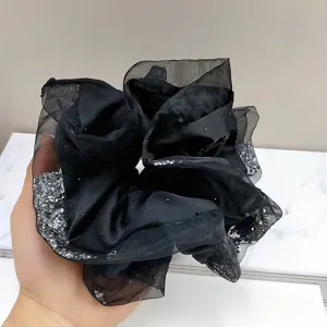 Detailed view of a luxury black satin scrunchie featuring sparkling organza edges and rhinestones