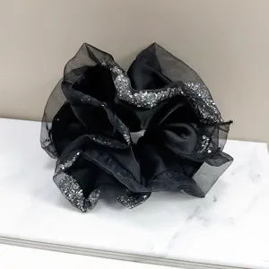 Detail view of black satin scrunchie with sparkling rhinestone edges on marble