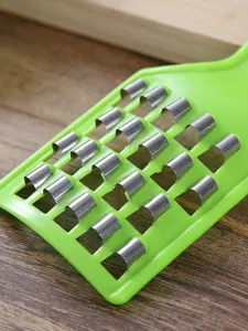 Primer plano de un rallador de repollo manual verde con cuchillas metálicas para cocina