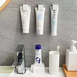 Wall-mounted white plastic clips for toothpaste and facial cleanser storage in bathrooms