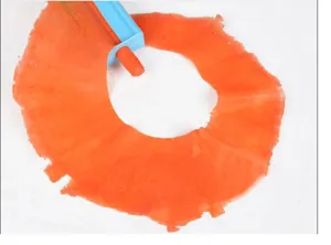 Detailansicht eines manuellen Gemüsehobels, der dünne orangefarbene Scheiben schneidet.