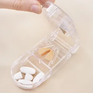 Compact transparent pill cutter and storage box shown with hand using the metal blade