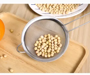 Primer plano de un colador de malla fina de acero inoxidable filtrando soja en una cocina