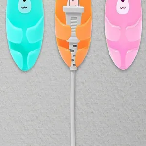 Close-up of colorful cartoon bear wall hooks organizing power plugs on a grey wall texture