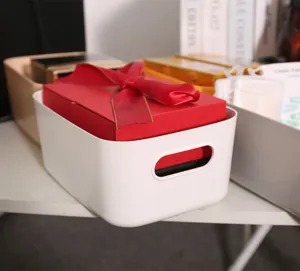 Caja de almacenamiento de plástico blanco con asas que contiene un regalo en un escritorio