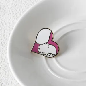 Detailed macro view of pink heart-shaped breastfeeding enamel brooch on a white saucer