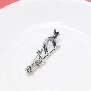 Close-up of a silver-toned flying cat on a broomstick brooch with crystal accents
