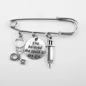 Detailed view of the syringe and stethoscope charms on the silver safety pin brooch