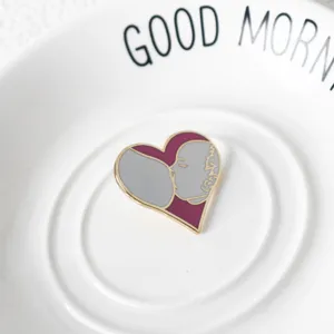 Detailed macro view of heart-shaped breastfeeding enamel pin on a white plate.
