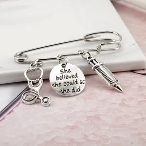 Detail of silver medical brooch with stethoscope, syringe and inspirational quote charm.