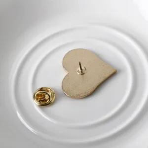 Detail view showing the golden back and butterfly clutch of a heart shaped alloy pin