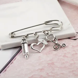 Silver medical brooch with syringe, nurse hat, and stethoscope charms on white marble