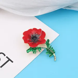 Detail shot of an elegant red poppy brooch with green leaves and a black center stone.