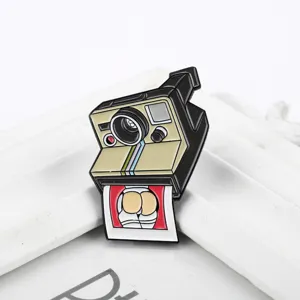 Primer plano de un pin de cámara esmaltado con un divertido diseño de foto de dibujos.