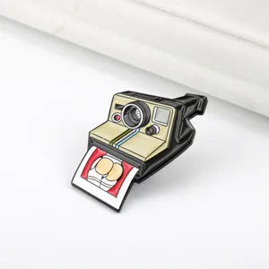 Primer plano de un pin esmaltado de cámara Polaroid retro con un divertido dije
