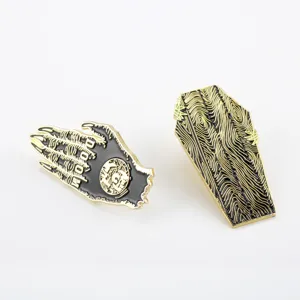 Detail of Halloween enamel pins featuring a black doom hand and a golden wood grain coffin