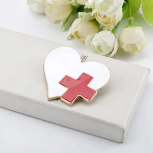 Dettaglio ravvicinato di spilla medica a forma di cuore con croce rossa e smalto bianco