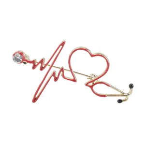 Detail view of a gold-tone stethoscope heart brooch with red enamel and rhinestone.