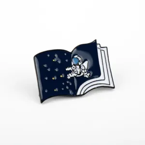 Detail of a cartoon magical book enamel pin featuring an astronaut and stars.