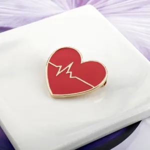 Detailed view of a red heart-shaped brooch with golden heartbeat line on a white marble slab
